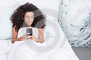 High angle view of african american young woman using smartphone in bed during morning time