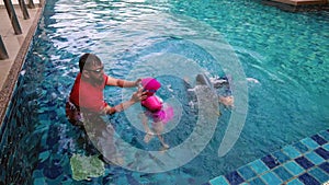 High angle view of asian family having fun in swimming pool outdoors. Active kids. Footage may contain noise due to low light