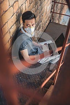 high angle view of asian teen in protective mask sitting with laptop on staircase air