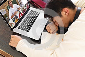 High angle view of asian teenage boy sleeping in front of laptop during online lecture at home