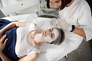 High angle view of beautician applying an alginic mask on a beautiful woman face at spa clinic