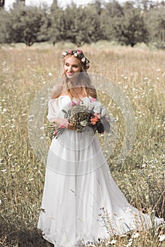 high angle view of beautiful smiling young bride in floral wreath and wedding dress holding bouquet of flowers and looking away