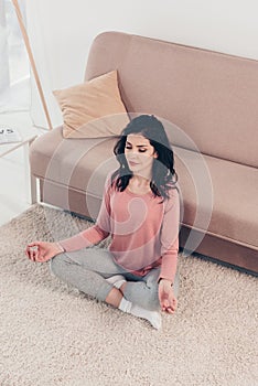 High Angle View of beautiful woman in Lotus Pose practicing meditation at home in Living Room.