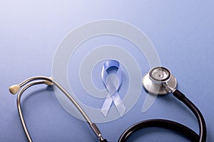 High angle view of blue stomach cancer awareness ribbon and stethoscope on blue background