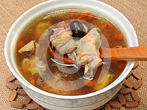 High angle view of a bowl of chicken soup on bamboo mat. It contain Chinese medicine such as goji berry and red jujube.