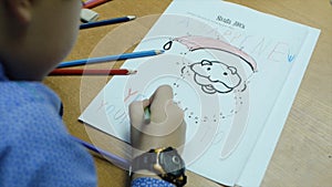 High angle view of boy drawing with color pencil on paper at desk in classroom. Clip. A cute little boy drawing with a