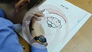 High angle view of boy drawing with color pencil on paper at desk in classroom. Clip. A cute little boy drawing with a