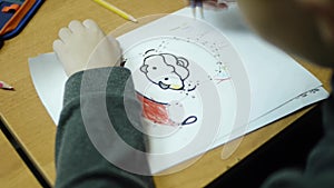High angle view of boy drawing with color pencil on paper at desk in classroom. Clip. A cute little boy drawing with a