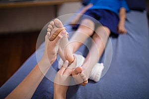 High angle view of boy lying on bed receiving foot massage from female therapist