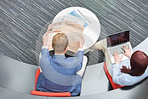 High angle view of businessman reading newspaper while female colleague using laptop in office