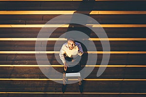 High angle view of businessman sitting on stairs, working on laptop and showing thumbs up at sunset