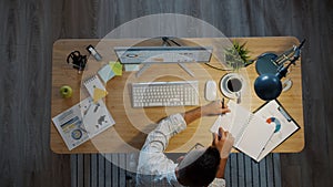 High angle view of businessman working at table in office writing in notebook looking at computer screen