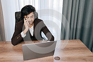 High-angle view of busy businessman talking smartphone typing laptop multitask in desk, looking to screen. Successful