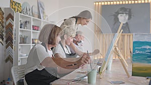 High angle view of cheerful senior friends painting on canvas. Senior woman smiling while drawing with the group