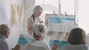 High angle view of cheerful senior friends painting on canvas. Senior woman smiling while drawing with the group