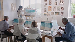 High angle view of cheerful senior friends painting on canvas. Senior woman smiling while drawing with the group