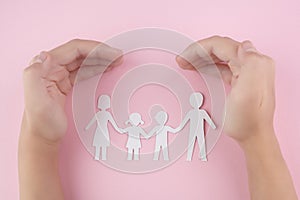 High Angle View Of Child Hand Protecting Family Papercut On pink background