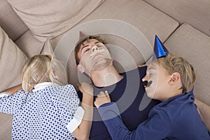 High angle view of children and father with artificial mustache and party hat sleeping on sofa bed