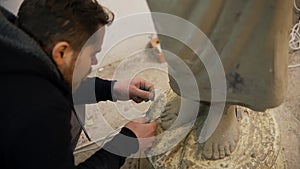 High angle view of clay Buddha's statue feet, artist works with detail using tools