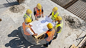 High-angle view of a construction team discussing architectural blueprints on site.