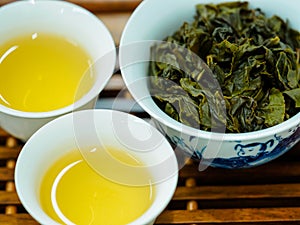 High angle view of cups of green oolong tea and tea leaves on a wooden tray