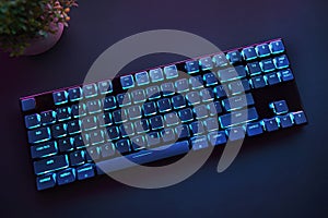 High angle view of cyan backlighted gaming computer keyboard laying on desk