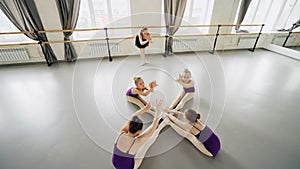 High angle view of diligent little ballet dancers practising forward bends sitting on floor in studio stretching and