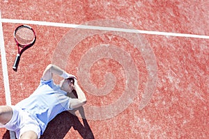 High angle view of disappointed mature man with head in hands while lying by tennis racket on court during summer