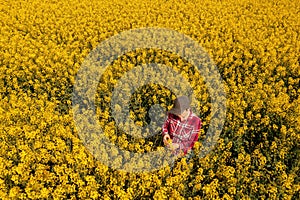 High angle view of female farmer examining rapeseed crops in bloom. Agronomist wearing red plaid shirt and trucker's hat is