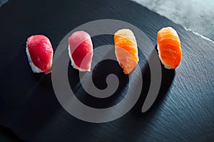 High angle view of four sushi portions laying on black textured board. Lights and shadows effect