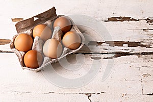 High angle view of fresh brown eggs in carton on white wooden table