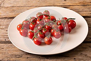 High angle view of fresh red cherry tomatoes in white plate on wooden table