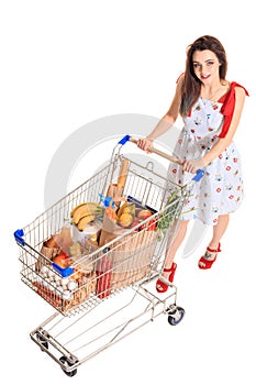 High angle view of girl smiling at camera while pushing a shopping cart full with groceries isolated on white background