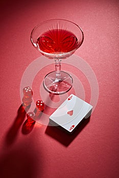 High angle view of glass of cocktail near deck of cards and dice on red background