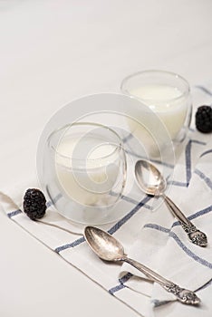High angle view of glasses of homemade yogurt, teaspoons and blackberries on cloth