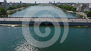 High angle view of glittering water surface reflecting sunshine. Tilt up reveal of Queen Louise Bridge, lake lined by