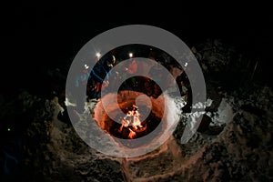 high angle view of group of tourists sitting and bask around a campfire in winter evening.