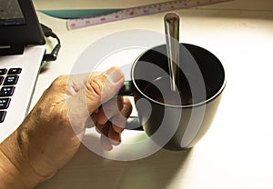 High angle view of hand holding a cup of black coffee on a white table in a house during working at home. Work from home concept