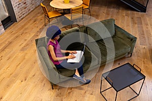 High angle view of happy biracial casual businesswoman with blue afro using laptop in office lounge