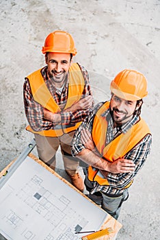 high angle view of happy builders with blueprint standing at construction site and looking