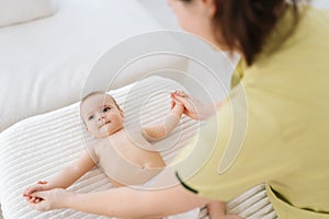 High-angle view of happy infant baby boy lying in bed playing with mom at home. Caring young mother doing gymnastic