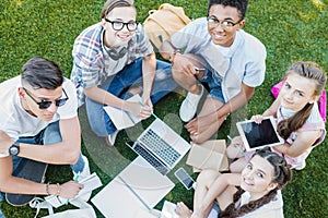 high angle view of happy multiethnic teenage students studying with books and digital devices