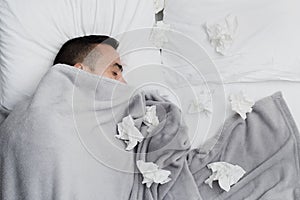 Ill man in bed surrounded by used tissues photo