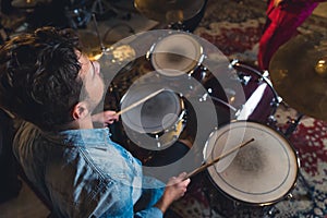 High angle view of male drummer using his wooden sticks. Concert and rehearsal of a garage band. Caucasian man in denim