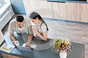 high angle view of married couple with cups of coffee using laptop together at counter