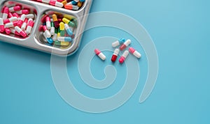 High-angle view of multi-colored antibiotic capsule pills on stainless steel tray and blue background. Antibiotic drug resistance