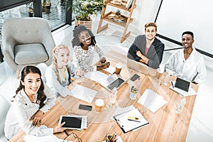 high angle view of multicultural group of business people looking at camera while sitting at table