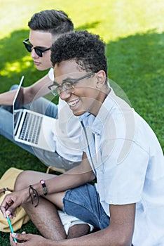 high angle view of multiethnic teenagers smiling and using laptop while studying together