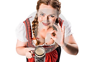 high angle view of oktoberfest waitress in traditional bavarian dress holding mug of dark beer and showing ok sign