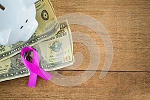 High angle view of paper currency and pink Breast Cancer Awareness ribbon by piggybank on wooden tab